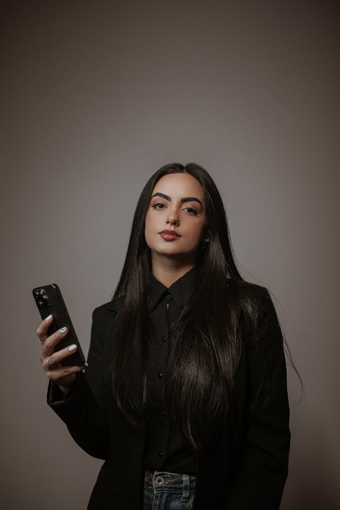 About Elegant woman in black clothing using a smartphone in a studio setting.