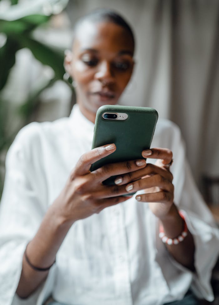 Home A woman in a white blouse using her smartphone indoors, showing a thoughtful and calm mood.