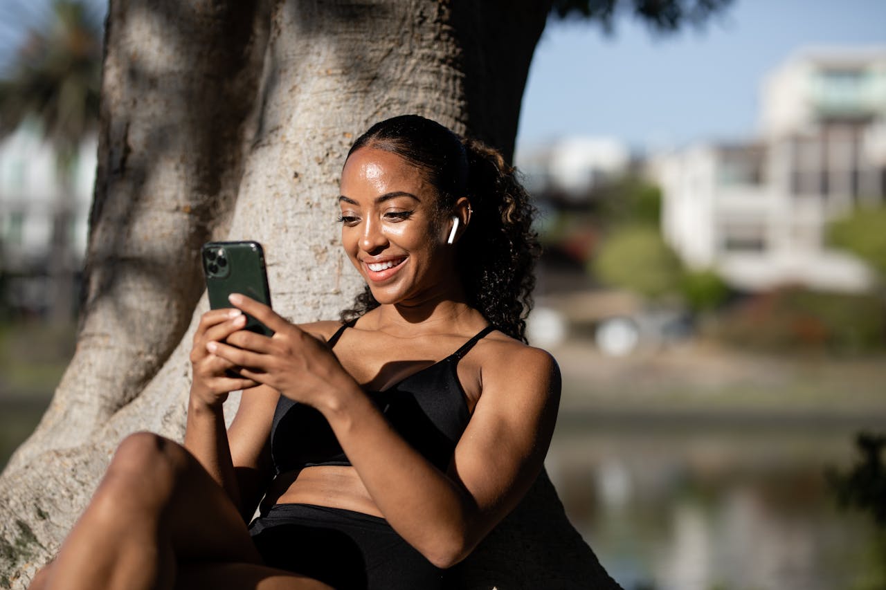 Mastering the First Impression: Your intriguing post title goes here A happy woman sitting under a tree, texting on her smartphone while enjoying the sunny outdoors.