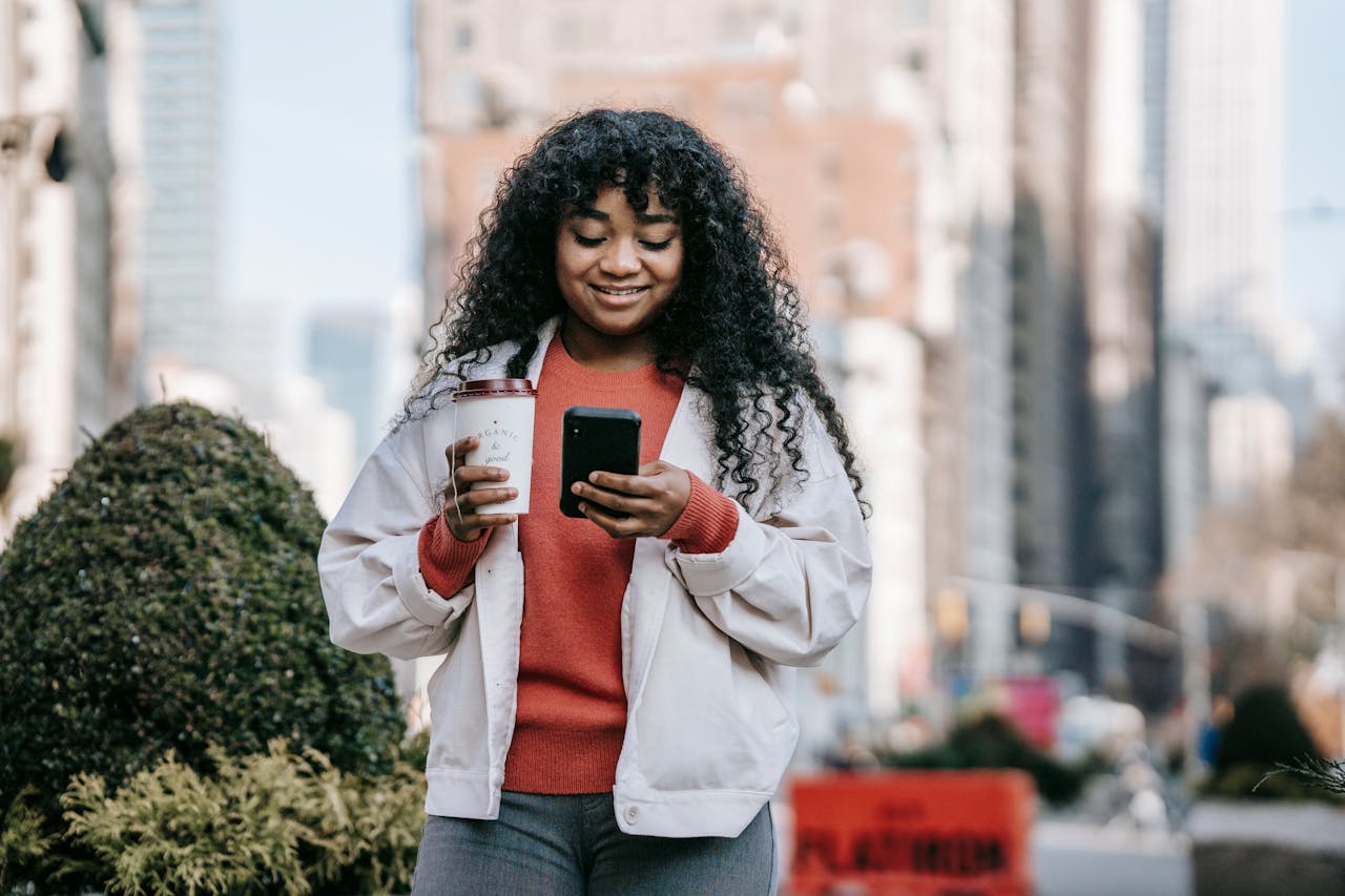 About Cheerful woman with a drink using a smartphone in a bustling urban environment.