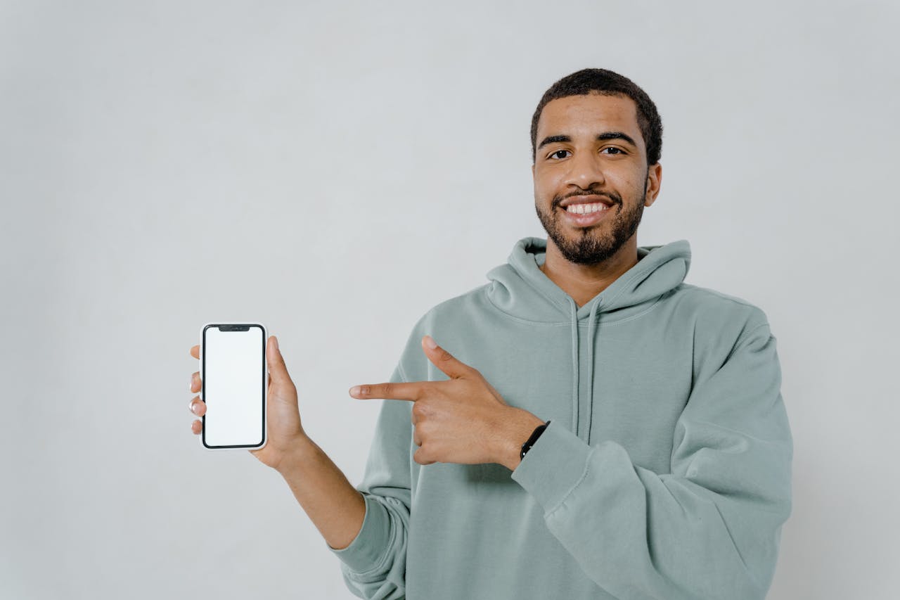 The Art of Drawing Readers In: Your attractive post title goes here A smiling man in a hoodie points at a smartphone with a blank screen, ideal for mockup or design use.